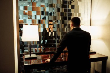 Takım elbiseli iş adamı odada aynaya bakıyor.