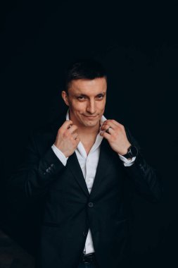 Stüdyoda koyu renk arka planda poz veren şık giyinmiş yakışıklı genç bir adamın portresi.         