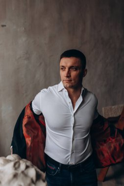 Stüdyoda poz veren genç bir adamın portresi, gömlek ve kot pantolon giyiyor.