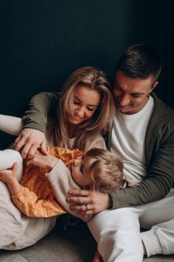 Beyaz kadın ve erkek, yeni yürümeye başlayan kızlarına sarılıyorlar. 