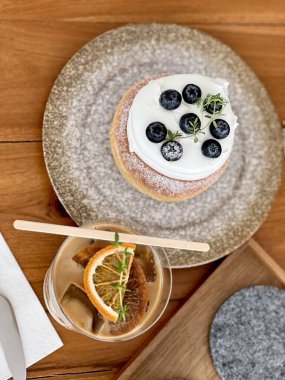 Minimalist bir kafede yaban mersinli, taze sütlü ve güzel dekore edilmiş portakallı kahveyle kaplanmış yabanmersinli kek. Tahta masaya yerleştirilmiş.