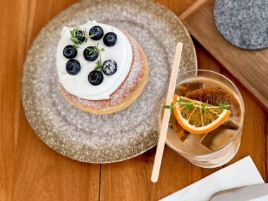 Yaban mersinli kek, minimalist bir kafede yakın plan. Üzeri yaban mersinli, taze sütlü ve güzel dekore edilmiş portakallı kahve.. 