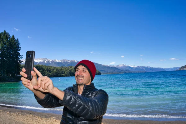 Posing for a selfie with a cell phone in front of a lake in Patagonia. High quality photo