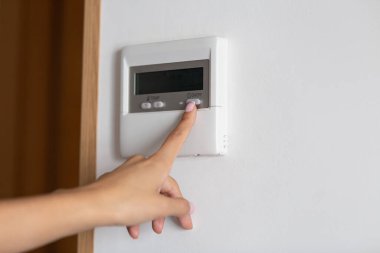 Klima ya da ısıtıcının açma kapama düğmesine basan genç bir kadının eli.