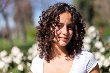 Parktaki kıvırcık saçlı genç kadın güneşin tadını çıkarıyor. 