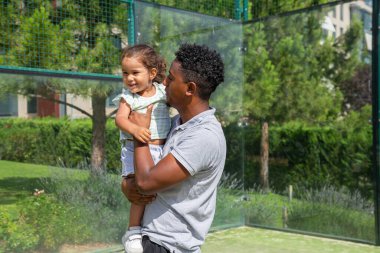 Loving black father with cute daughter on sports ground 