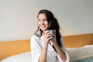 Young woman drinking coffee in bed in bathrobe 