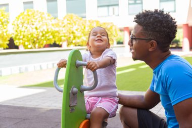 Father playing with his daughter on a pony swing in the park 