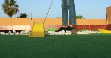 Close-up of unrecognizable woman hitting ball with golf club in mini golf 