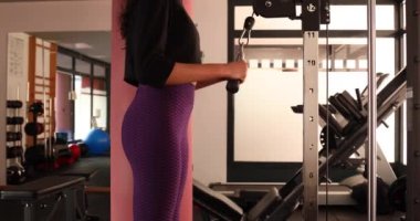 Spor salonunda makara makinesiyle triseps egzersizi yapan genç bir kadın. 
