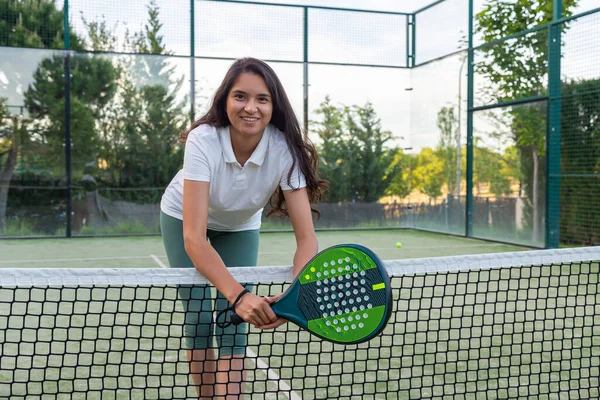 Gülen genç İspanyol kadın Padel kortunda raketle poz veriyor.