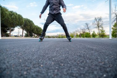 Spor giyimli, kimliği belirsiz, genç ve havalı bir erkek paten sürerken parkta çok hızlı yol alır.