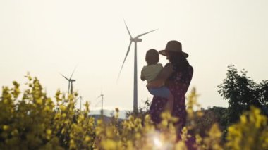 Kollarında kızı olan bir anne yel değirmeni çiftliğine bakıyor. İnsanlar ve doğa koruma kavramı, ekolojik enerji kaynakları, rüzgardan gelen elektrik. Yüksek kalite 4k görüntü