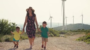 Anne, çocuklarla dağlarda yel değirmenlerinin yanında yürüyor. Çevre koruma, elektrik koruma ve ekolojik rüzgar enerjisi kavramı. Yüksek kalite 4k görüntü