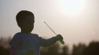 Gün batımında sabun köpüğü üfleyen bir çocuğun yavaş çekim videosu. Çocukların mutluluk, samimiyet, özgürlük ve samimiyet kavramı. Yüksek kalite 4k görüntü