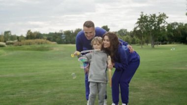 Bir aile parkta birlikte sabun köpüğü üflüyor. Anne, baba ve oğul doğada birlikte eğleniyorlar. Geniş aile kavramı. Yüksek kalite 4k görüntü
