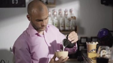 Erkek bir barista bir fincan kahveye ılık süt döker. Bir profesyonel kafede cappuccino ya da latte hazırlar. Yüksek kalite 4k görüntü