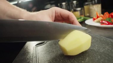 Kesme tahtasındaki patatesleri dilimleyen bıçağın yavaş çekim videosu. Profesyoneller mutfakta yemek pişiriyor. Yüksek kalite 4k görüntü
