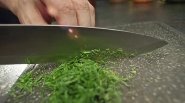 Kesme tahtasındaki bıçakla dereotu dilimlerken yavaş çekim videosu. Mutfakta salata hazırlama süreci. Yüksek kalite 4k görüntü