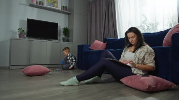 Eine Frau Arbeitet Computer Und Ihr Sohn Spielt Wohnzimmer Mit — Stockvideo