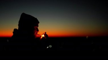 Gün batımında sigara yakan bir adamın silueti. Bir adam sigara içer ve güzel bir manzarada düşünür. Sigara insanları öldürür ve zararlı indirimler yapar. Yüksek kalite 4k görüntü