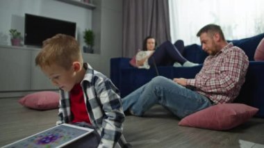 Yaşam tarzı video ebeveynleri evde çalışır ve çocuk tablette oynar. Aile oturma odasında aletlerle birlikte oturur. Yüksek kalite 4k görüntü