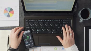 Ofiste dizüstü bilgisayarla çalışan bir adamın yakın çekimi. İş adamı mesaj yazıyor ve iş yerindeki telefona bakıyor. Yüksek kalite 4k görüntü