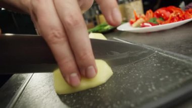 Kesme tahtasındaki patatesi kesen bıçağın yavaş çekim videosu. Mutfaktaki aşçının tabaklar için hazırladığı malzemeler. Yüksek kalite 4k görüntü