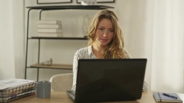 Ofiste dizüstü bilgisayarda yazı yazan beyaz bir kadın. Kız yapılan işten memnun kaldı. Evde internetten etkileyici bir serbest yazar çalışması. Yüksek kalite 4k görüntü