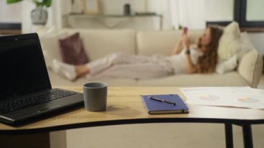 The girl is resting on the sofa using the phone with social networks after a hard day at work. Home office with computer and documents on the table. High quality 4k footage