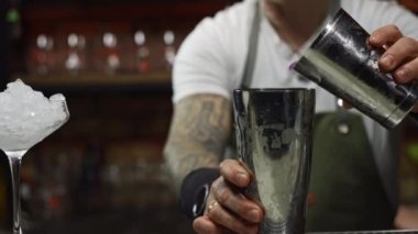 Slow motion video of a bartender making a cocktail at a bar for a party. The bartender pours alcohol from the shaker and hits it with his hand. High quality 4k footage