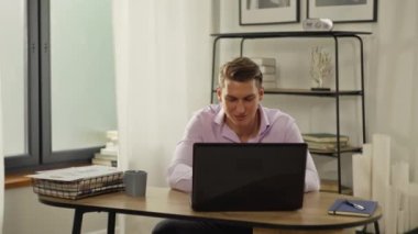 A businessman finishes work on a project and leans back in his chair. The manager smiles and rejoices after a successfully completed job. Remote work online from home. High quality 4k footage