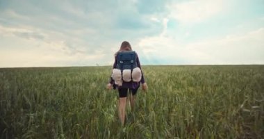 A woman travels with a backpack while hiking in a field. A girl alone feels freedom and happiness. Beautiful landscape nature protection. High quality 4k footage