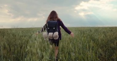 A woman is hiking with a backpack on a green field. A dreamy girl walks in nature and feels pleasure and freedom. High quality 4k footage