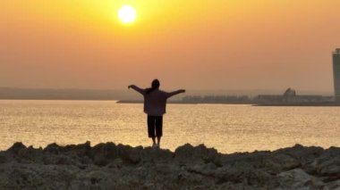Hava manzaralı kadın ellerini kaldırır ve okyanusta gün batımında sevinir. Kumsalda zaferi kutlayan başarılı bekar kız. Yüksek kalite 4k görüntü