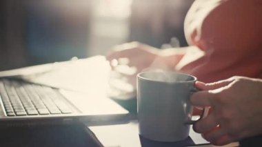 Beyaz bir kadın bilgisayar klavyesine yazı yazıyor, bir fincan kahve alıyor ve içiyor. Sabah içkisi. Ev sahibi iş kadınından uzaktan kumanda. Yüksek kalite 4k görüntü