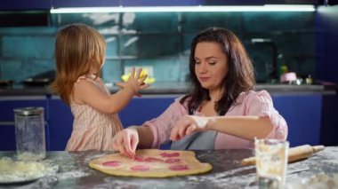 Kız, annesinin evdeki mutfakta pizza yapmasına yardım ediyor. Aile evde birlikte çalışıyor. Mutlu bir ailenin yaşam tarzı. Yüksek kalite 4k görüntü
