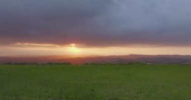 Güneşin battığı yerdeki dağların arka planına sahip yeşil tarım arazilerinin havadan görünüşü. Doğadaki güzel günbatımı manzarası. Yüksek kalite 4k görüntü