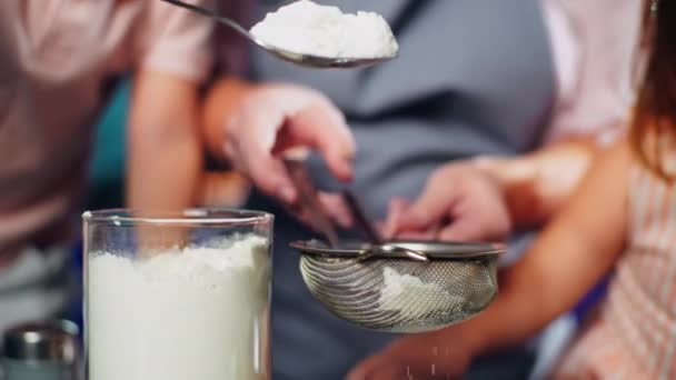 母親が小麦粉をふるいにかけるのを助ける子供の手のクローズアップ 自宅のキッチンで家族としておいしいペストリーを調理します 高品質4K映像 — ストック動画