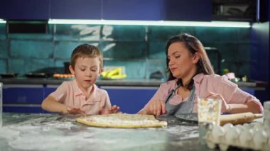 Beyaz bir aile mutfakta pizza hazırlıyormuş. Çocuk pizzayı deniyor ve çok lezzetli olduğunu gösteriyor. Birlikte çalışmak, evde annemle yemek pişirmek. Yüksek kalite 4k görüntü