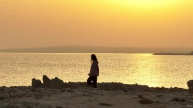 Gün batımında deniz kıyısında yürüyen hayalperest romantik bir kadının hava manzarası. Tatilde olan bir kız okyanusun dalgalarına bakarak rahatlar ve meditasyon yapar. Yüksek kalite 4k görüntü