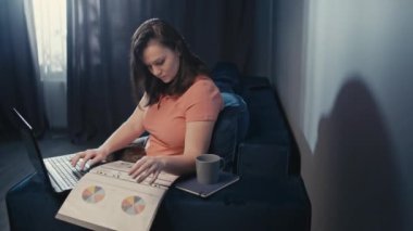 İnternette çalışan Avrupalı bir kadın. Bir iş kadını, bir dairedeki kanepede otururken belgelere bakar ve bilgisayara bakar. Yüksek kalite 4k görüntü