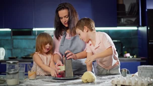 母親と子供はピザにチーズをこする 家族は台所で一緒に夕食を準備しています 一緒に幸せな親と娘と息子の明るい笑顔 高品質4K映像 — ストック動画