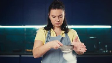 Kafkasyalı bir kadının süzgeçten un geçirdiği yavaş çekim videosu. Kız ev mutfağında lezzetli hamur işleri ve tatlılar hazırlıyor. Yüksek kalite 4k görüntü