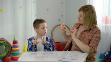 Beyaz bir çocuk sınıfta konuşma terapistiyle birlikte çalışıyor. Çocuk bir profesyonelle harfleri ve sesleri doğru telaffuz etmeyi öğreniyor. Yüksek kalite 4k görüntü