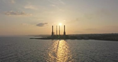 Gün batımında deniz kıyısındaki hava görüntüleme güç istasyonu. Borulardan çıkan duman havayı CO2 ile kirletiyor, dizelden elektrik üretiliyor. Zararlı gazların atmosfere yayılması. Gezegeni kurtarmak. 