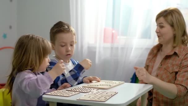 先生は幼稚園のテーブルで子供たちと論理的なゲームをしています 男の子と女の子は仕事をしてる賢い子供の世代 高品質4K映像 — ストック動画