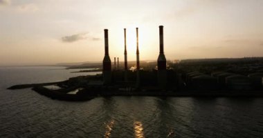 Gün batımında deniz kıyısındaki enerji santralinin havadan görüntüsü. Borulardan gelen duman havayı ve çevreyi kirletiyor. Ekosistemin ve doğanın korunması. Yüksek kalite 4k görüntü