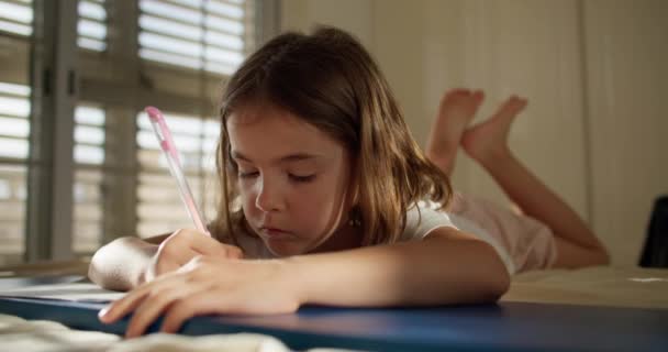 Uma Criança Escreve Com Uma Caneta Caderno Enquanto Está Deitada — Vídeo de Stock
