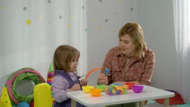 Bir öğretmen anaokulunda bir kızla mantık geliştirmek için oyunlar oynar. Çocuk renkleri inceler, tahmin eder ve bir bulmaca oluşturur. Mutlu çocukluk ve akıllı çocuk kavramı. 